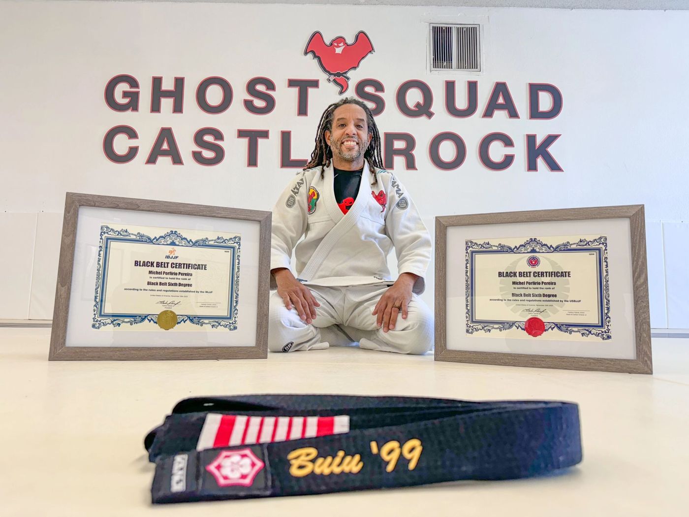 Master Michel 'Buiu' Porfirio Pereira kneeling with his black belt certificates and 1999 black belt