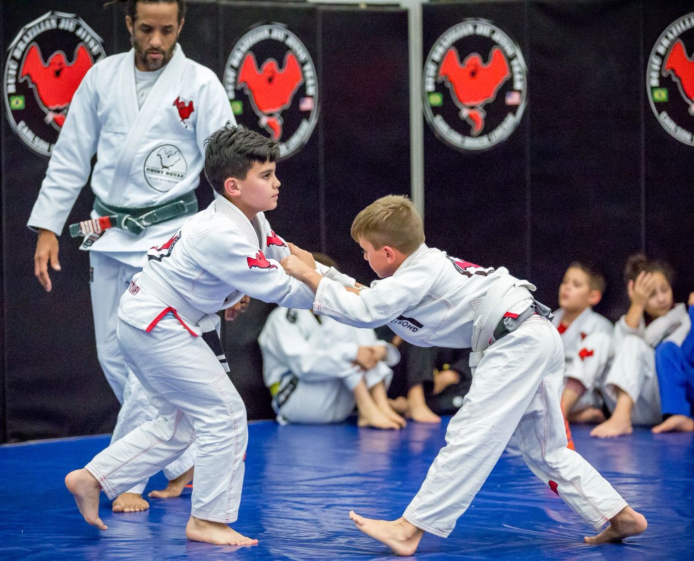 Two kids practicing takedowns in gi during kids class